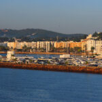 Scenic view of Santa Eulalia, Ibiza, featuring a vibrant marina, luxury yachts, and a coastal skyline at sunset