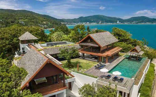 Aerial view of luxury hillside villas with private pools overlooking tropical greenery and ocean in Phuket, Thailand.